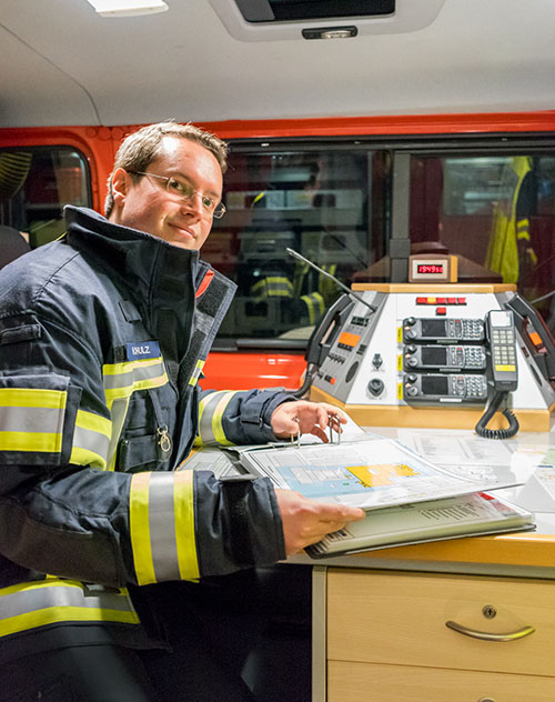 Henrik Schulz in Einsatzkleidung im Einsatzleitwagen, an der Funkkonsole mit Kartenmaterial